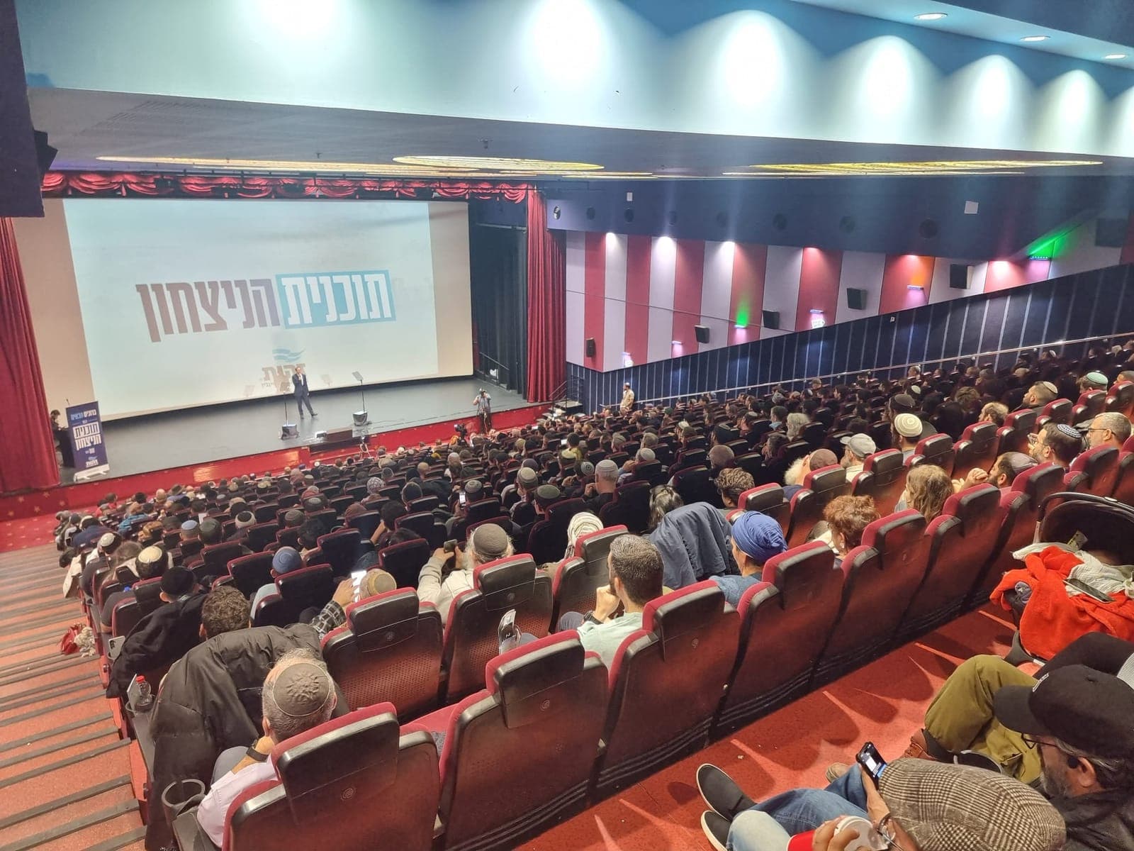 אולם קולנוע מלא במאות משתתפים בכנס "תוכנית הניצחון" של זהות, שם הכנס מוקרן על המסך